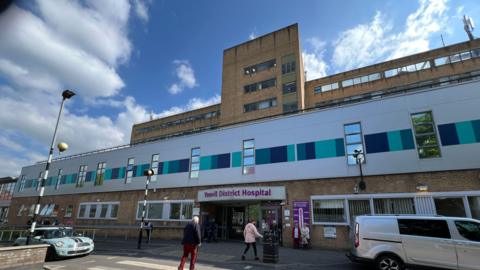 The external entrance to Yeovil District Hospital, with people walking in and cars going past. 