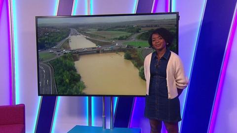 Emma-Louise in the studio with a picture of flooding in the screen.