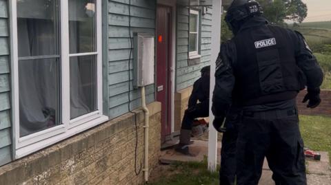 Police picture of a raid on a house. Two officers are visible in protective uniform gaining entry via the front door