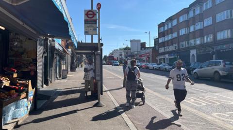 So-called floating bus stop shows the shelter, a cycle lane and the bus stop itself. A woman with a pushchair is awaiting a bus
