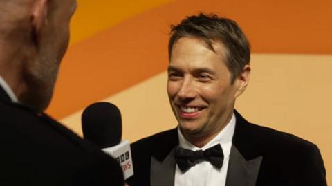 Sean Baker wearing a suit and bowtie smiling