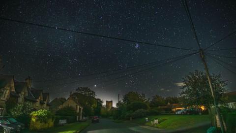 A dark sky full of stars over a rural village with church tower in the background