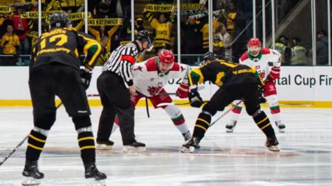 Cardiff Devils and Katowice players at a face-off with referee about to drop the puck