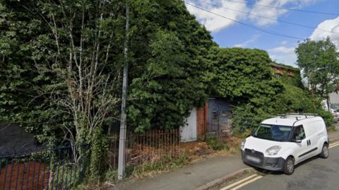 Street view of the former factory overgrown with vegetation