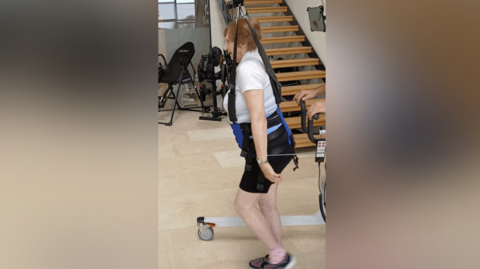 A woman in shorts and a T-shirt being suspended by a harness from a hoist