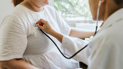 A doctor listens to the chest of an overweight lady using a stethoscope