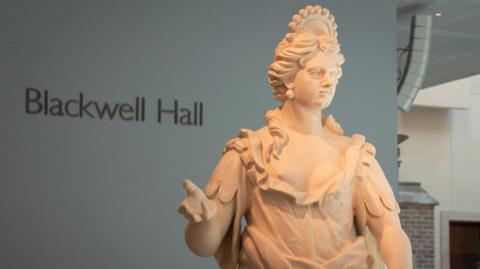 A close up of one of the stone muses in Blackwell Hall. She holds a hand out, one of her breasts is visible.