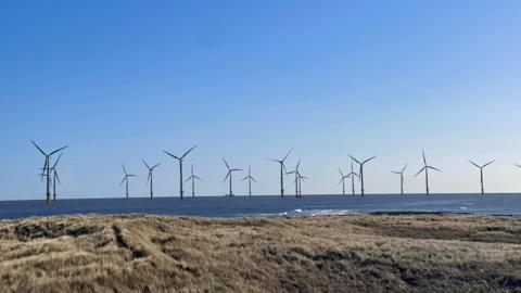 A sunny view of a number of wind turbines off Redcar beach.