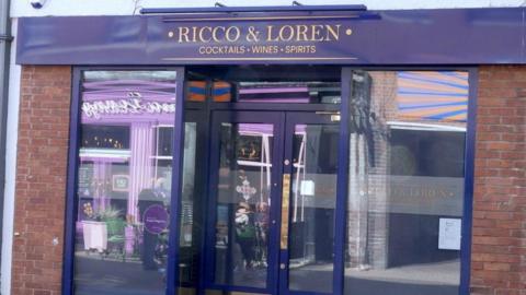 A shiny blue shop front with Ricco & Loren, cocktails wines sprits written in gold at the top of the doors.