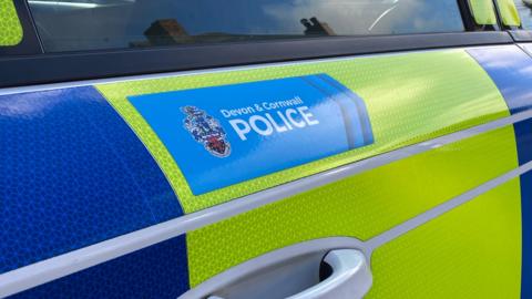 The reflective blue and yellow door of a Devon and Cornwall Police car.