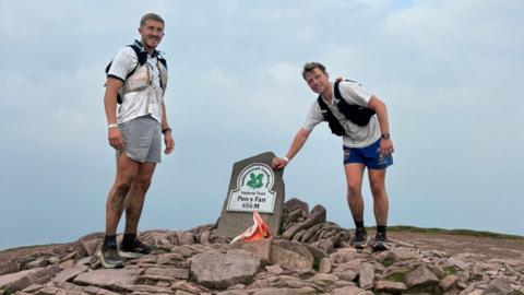Two male runners in white shirts and blue shorts at the top of Pen y Fan