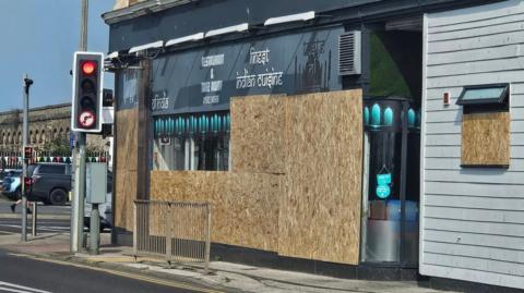 A photo showing the front of an Indian restaurant in Lowestoft. Large wooden boards can be seen covering majority of the restaurant's windows. 