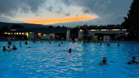 Swimmers in the outdoor pool at dusk 