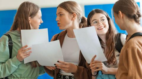 Four students standing talking all holding pages.