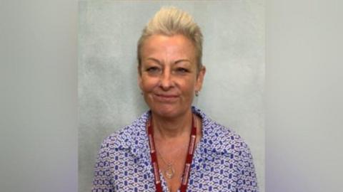 Gaynor is wearing a pattered blue and white shirt with a red council lanyard around her neck 