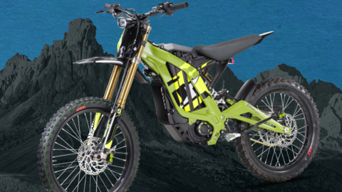 A lime green and black Sur-Ron Light Bee X electric motorbike with gold front suspension and off-road tyres, shown side-on against a mountain-style backdrop.