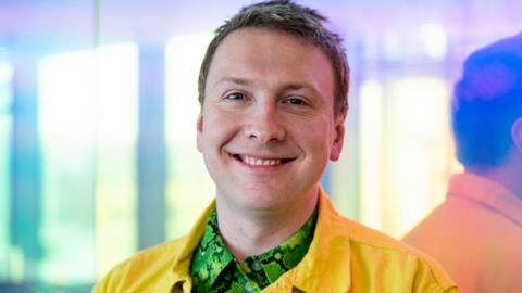 Joe Lycett at the BBC. Wearing yellow jacket and green snake print shirt