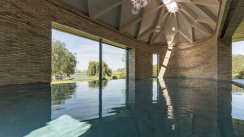 Water fills the inside of the structure that is visible, reaching perimeter walls and a large window. Trees, grass and water outside are in the background.