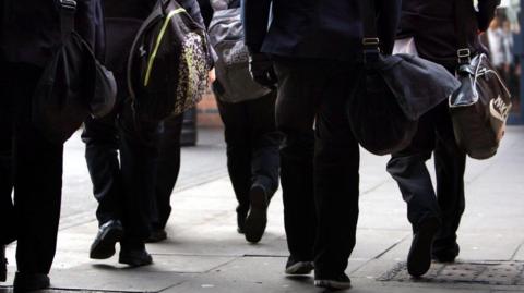 A generic image showing a handful of students, carrying bags, walking away from the camera. 