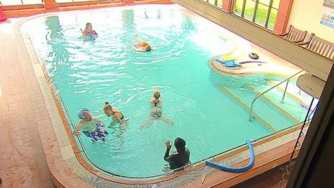 People swimming in a hydrotherapy pool. Its windows overlook marine lake in Southport.