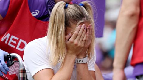 Molly Caudery covers her face with her hands as she's helped away from the track in a wheelchair