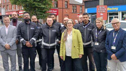 Group photo of Liverpool City Councillor Laura-Robertson-Collins and the new litter enforcement taskforce. They are posing and smiling for the camera while standing on the side of a road. 