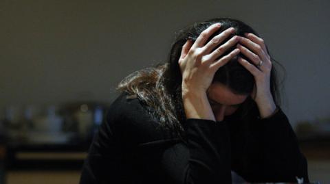 A woman with her head in her hands, sits in a dark room