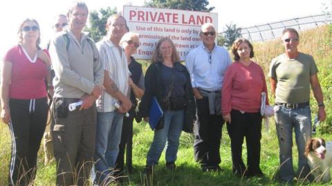 A group of a dozen people huddle together smiling in front of a sign reading "private land".