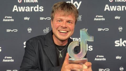 Max Klymenko holds up his tiktok award to the camera while posing on the red carpet