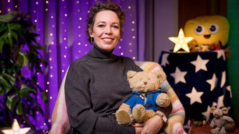 Olivia Colman sat in a chair holding a teddy bear