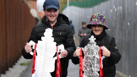 Two young fans hold tinfoil FA Cups before Stockport County v Brackley Town in the second round 