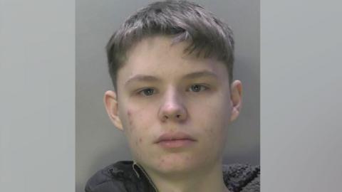 A mugshot of Thomas Waller. He is wearing a grey hooded top and looking at the camera. 