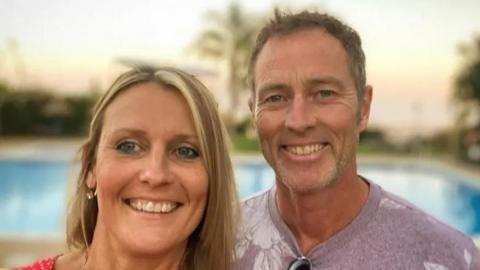 A selfie of Craig and Lindsay Foreman. Lindsay has blonde hair and Criag is wearing a pink t-shirt.