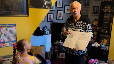 Clarke is being watched by daughter Dakota as he holds open an exercise book containing colourful pictures of Pokemon characters. 