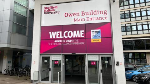 Sheffield Hallam University is a modern building with bright pink and purple branding which says Owen Building Main Entrance