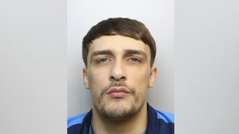 Man with a beard looking at the camera. It is a mugshot and he looks serious.