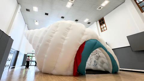 A large white fabric is designed to look like a sea shell and is able to fit 20 children inside