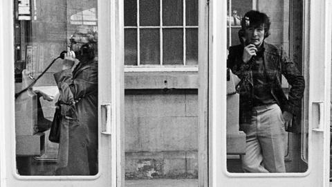 Two people in phone boxes