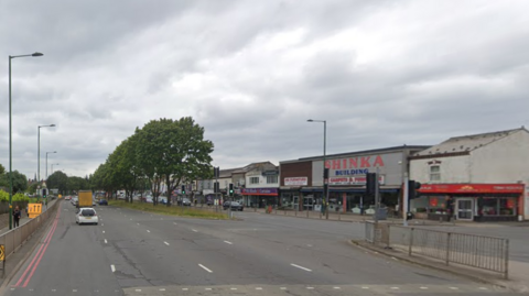 A multi-lane road with trees in the middle and businesses to the right