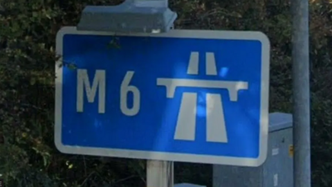 A blue M6 sign surrounded by bushes.