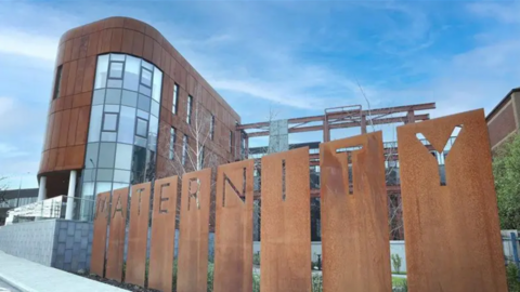 Tall glass and metal building with a large metal sign outside that spells out Maternity.