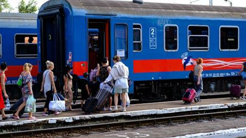 Ukrainian refugees carrying their belongings enter a blue train in Hungary. 