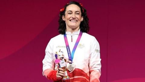 Sarah Davies Smale in a red and white England vest lifting weights above her head during the Commonwealth Games competition in Glasgow