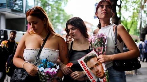 Young women look at flowers left outside hotel in Buenos Aires where Liam Payne died