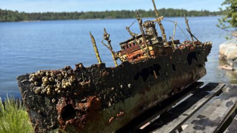 A model of a ship model that has been recovered from the sea. It is covered in barnacles and has rusted. 