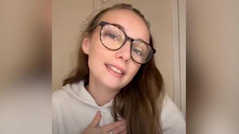A girl with a white hoody top with glasses and brown hair