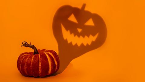 Orange pumpkin casting shadow with sinister face on yellow background.