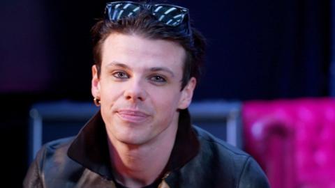 A head and shoulders image of Yungblud, who is wearing a leather jacket and sunglasses on his head while looking into the camera