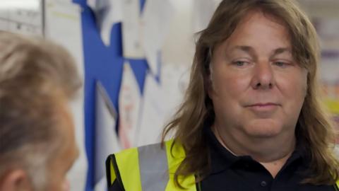 Man with long hair and high-vis jacket looking down