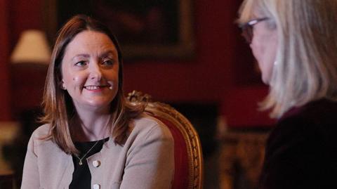 Kristina Penny with long brown hair wearing a beige smart cardigan with a black top. She is in Number 10 sitting on an ornate gold and red velvet chair talking to her aunt who has long blond hair wearing a black outfit to the right.